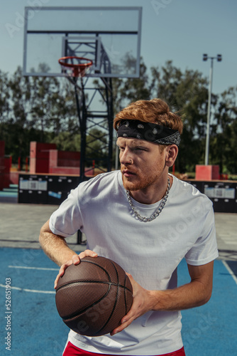 young sportsman in bandana and necklace playing basketball outdoors