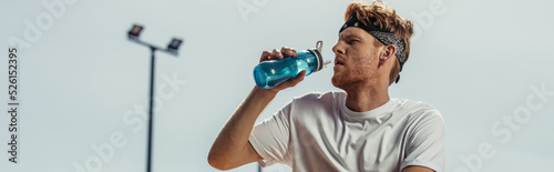young sportsman drinking refreshing water from sports bottle outdoors, banner