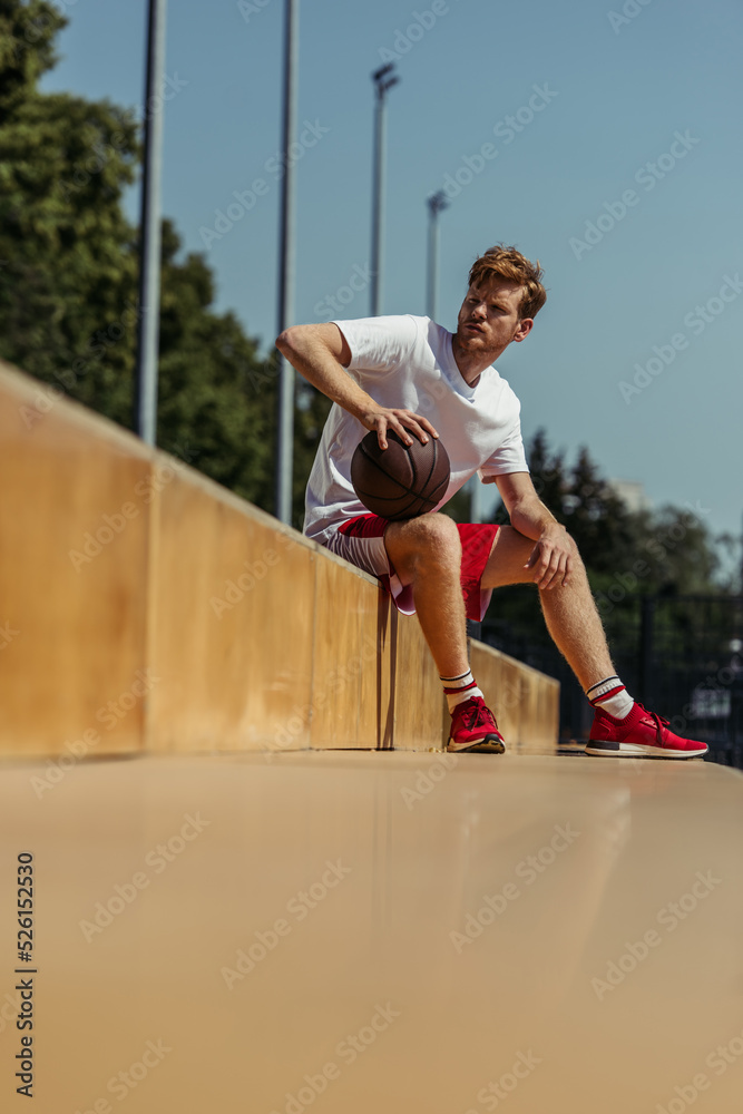 full length of man in red sneakers sitting on stadium with ball full length of man in red sneakers sitting on stadium with ball