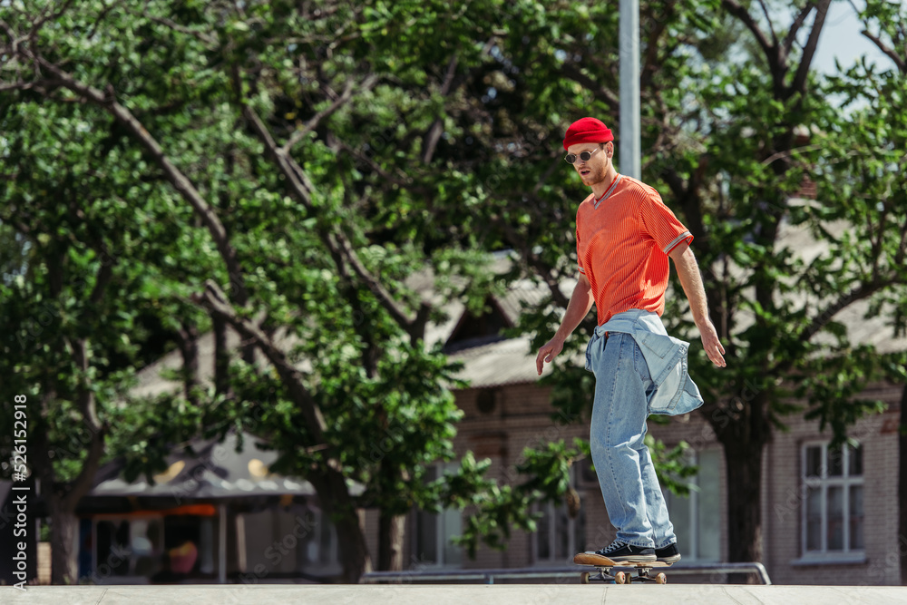 full length of man in stylish outfit skateboarding in blurred city park