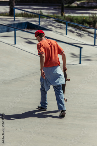 back view of man in red beanie walking with skateboard in skate park
