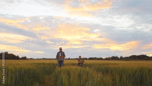 Farmer and his son in front of a sunset agricultural landscape. Man and a boy in a countryside field. Fatherhood, country life, farming and country lifestyle. © Acronym