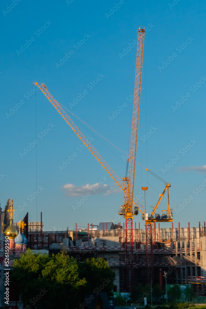 Yellow tower cranes and unfinished building construction against summer cloudy blue sky. Building process, architecture, urban, engineering, industrial and development concept