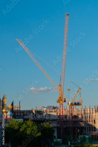 Yellow tower cranes and unfinished building construction against summer cloudy blue sky. Building process, architecture, urban, engineering, industrial and development concept