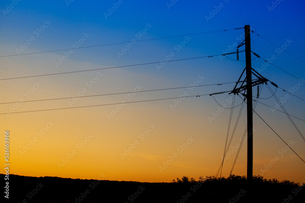 A tower with power lines from a nuclear power plant in Ukraine against the background of a sunset with the colors of the flag of Ukraine