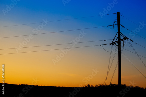 A tower with power lines from a nuclear power plant in Ukraine against the background of a sunset with the colors of the flag of Ukraine
