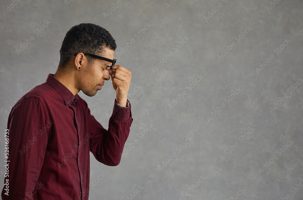 Profile view of a tired dark-skinned young man rubbing his eyes after doing hard work. Concept of eye fatigue from the computer and fatigue from work. Gray background. Place for text. Banner. Profile view of a tired dark-skinned young man rubbing his eyes after doing hard work. Concept of eye fatigue from the computer and fatigue from work. Gray background. Place for text. Banner.