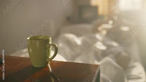 Cup with hot coffee or tea with steam on the table with blurred bed background.