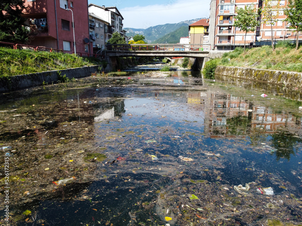 A polluted river in the city. Garbage in the river. Trash floating in water. Environmental problem. Plastic bags, bottles and garbage dumped in river. 