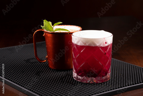 copper mug of moscow mule drink and berry drink with mint leaves seen from the front on the bar counter