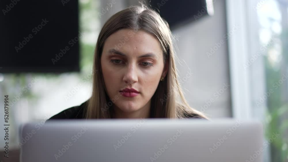 Young woman face looking at laptop computer seated at coffee shop. Portrait person browsing internet online in front of computer screen Young woman face looking at laptop computer seated at coffee shop. Portrait person browsing internet online in front of computer screen