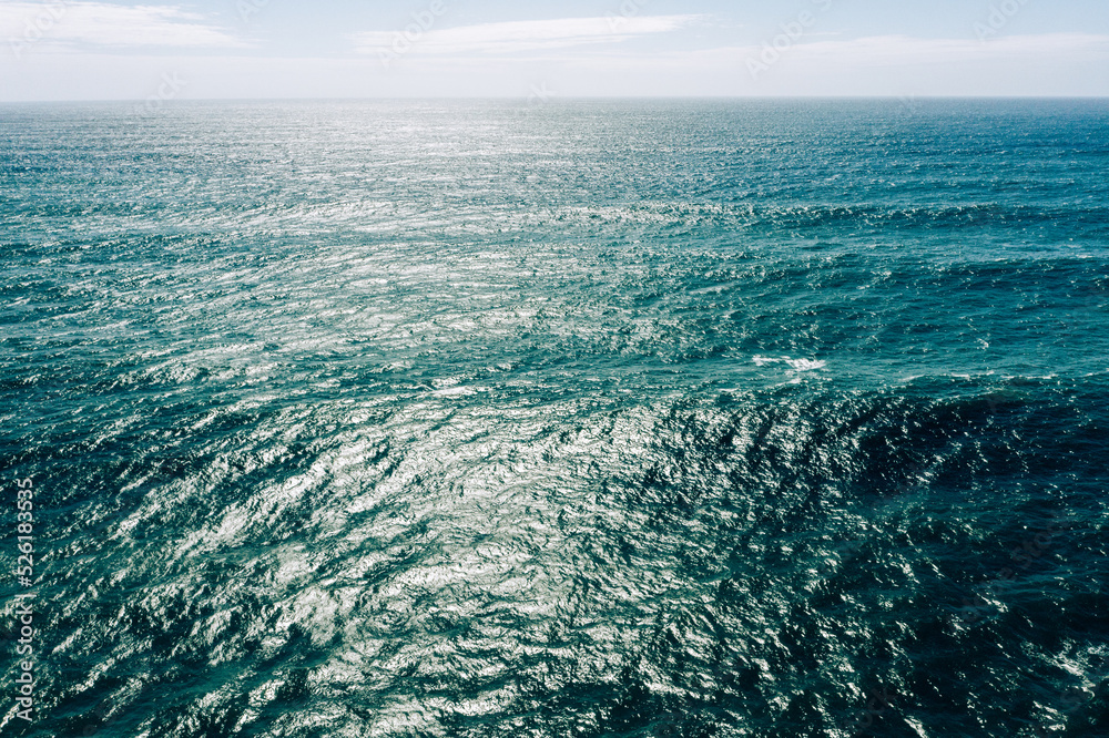 Aerial view over azure ocean with rolling waves. Top view to the ocean in summer sunny day - closeup. Drone view of a Scenic ocean waves. Beautiful Sea blue water with blue sky..