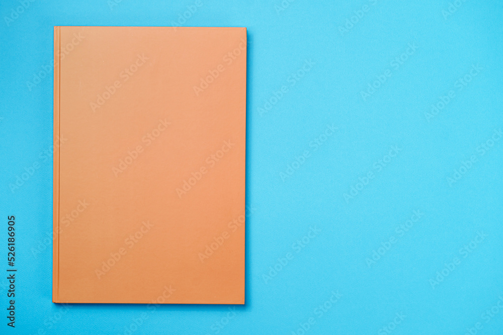 Fototapeta premium Orange Leather notebook on paper blue background, notepad mock up, top view shot