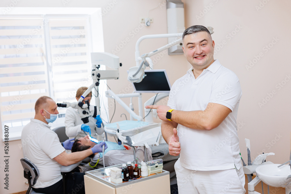 The dentist is in his dental office. A dentist in a white uniform treats a patient's teeth with a dental microscope. Dental office