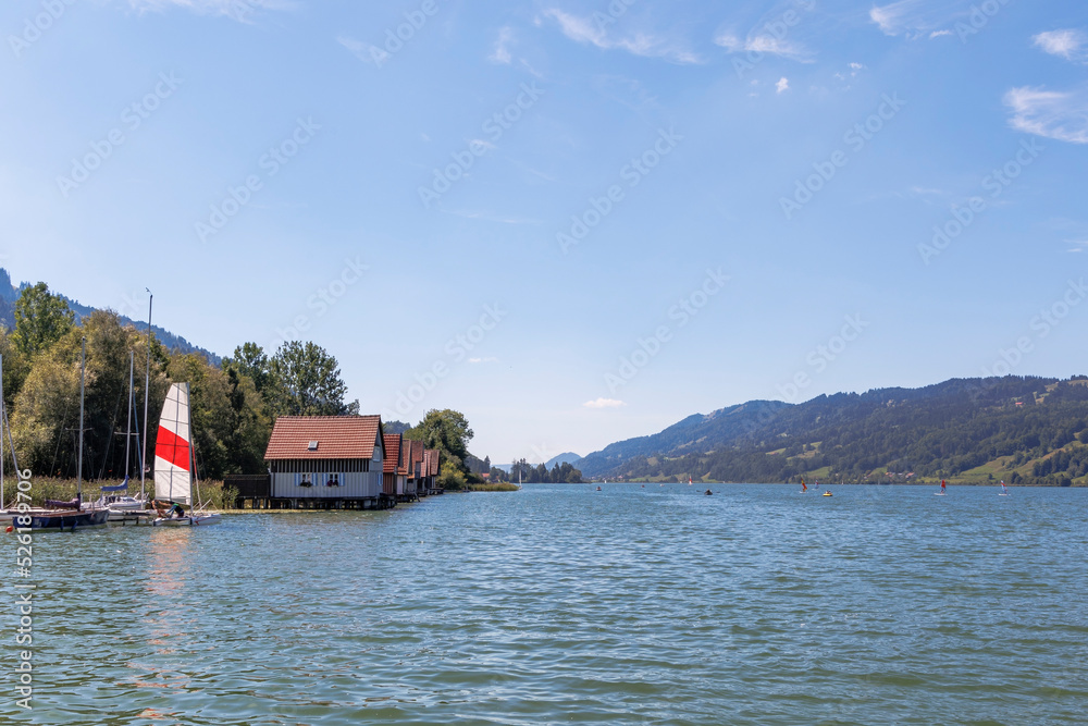 Colorful wooden boathouses with jetty at the Alpsee near Immenstadt