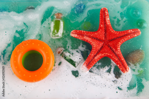 Top view on toy ocean in aquarium. Top view on blue watr with white foam, red starfish, stone, small glass bottle and round orange lifebuoy. Top view on storm, flatly photo