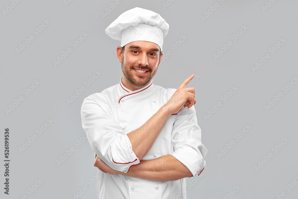 cooking, culinary and people concept - happy smiling male chef in toque pointing to something over grey background