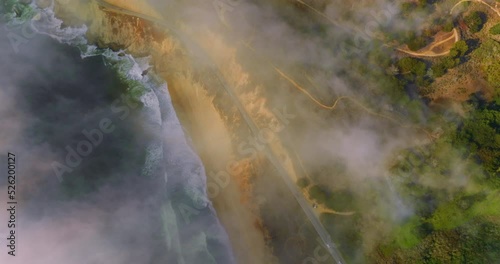 Rocky beach with waves coming back and forth. Highway with cars moving by in the mountainas. Amazing scenery covered with fog in Montara, California, USA. photo