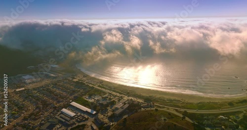 Huge wave of thick white fog moving from the ocean to the beach. Little residential area at the coastline of Montara, California, USA from aerial perspective. photo