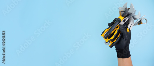 hand wearing black gloves hold different types of black yellow hand tools isolated blue background