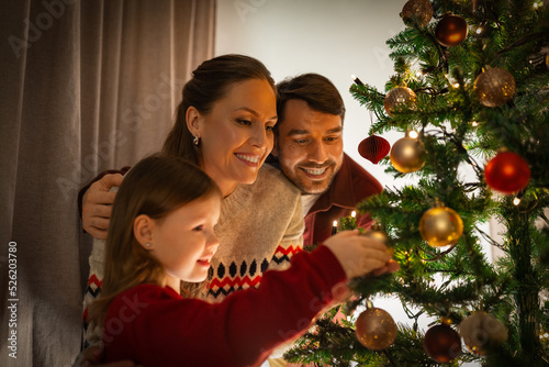 family, winter holidays and people concept - happy mother, father and little daughter decorating christmas tree at home