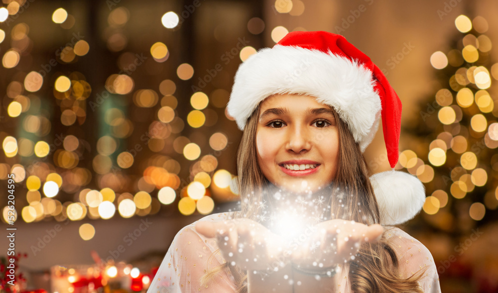 christmas, holidays and magic concept - happy smiling teenage girl in santa helper hat holding fairy dust over festive lights at home background christmas, holidays and magic concept - happy smiling teenage girl in santa helper hat holding fairy dust over festive lights at home background