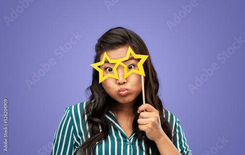party props, photo booth and people concept - woman with big glasses in shape of stars over violet background