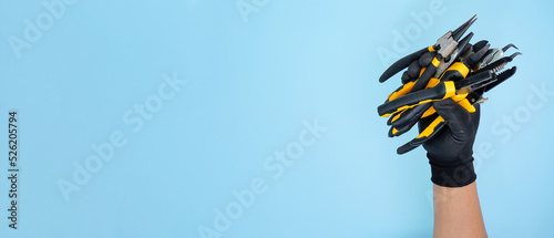 hand wearing black gloves holding different types of black yellow pliers isolated blue background
