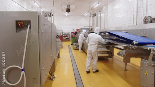 Workers in uniform supervise the operation of automatic line for production of meat products for retail