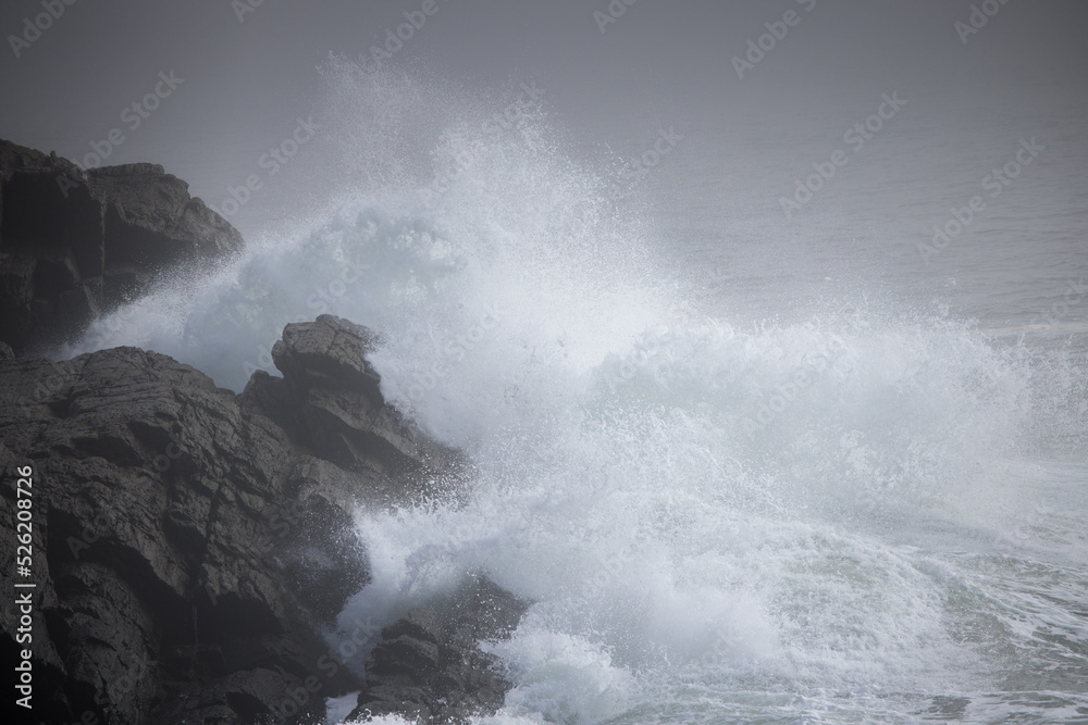 Ocean waves crashing onto a rocky shore on a foggy morning