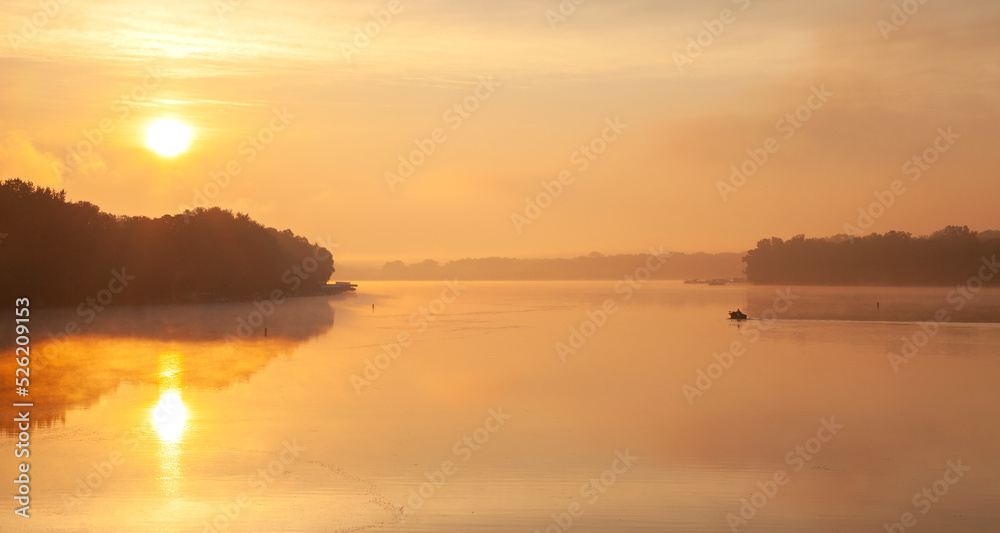 A fisherman heads out on a golden calm lake in Wisconsin at sunrise