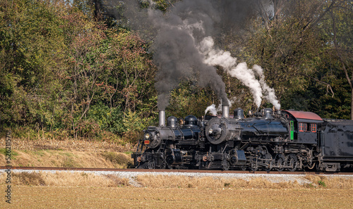A View of Two Steam Engines, blowing Smoke and Steam Warming Up Next to Each Other on a Sunny Day