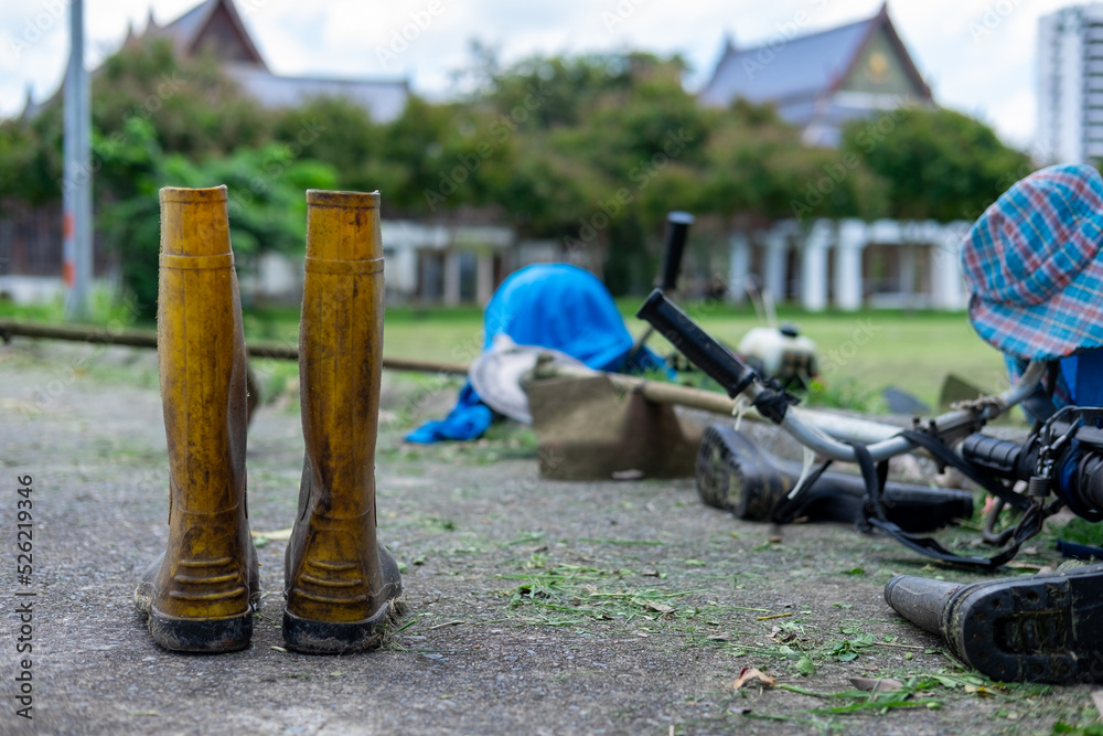 Naklejka premium A dirty yellow rubber boots on a curbside with other gardening tools