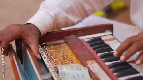 Closeup shot of hands of an Indian street performer playing Harmonium on the street at Jaisalmer in Rajasthan, India. Out of focus money on top of the Harmonium while man plays it. Indian culture.  photo