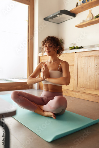 Yoga Meditation. Woman Practices Yoga In Easy Position At Home. Caucasian Girl With Fit Body In Sport Clothes Meditating On Yoga Mat Indoors 