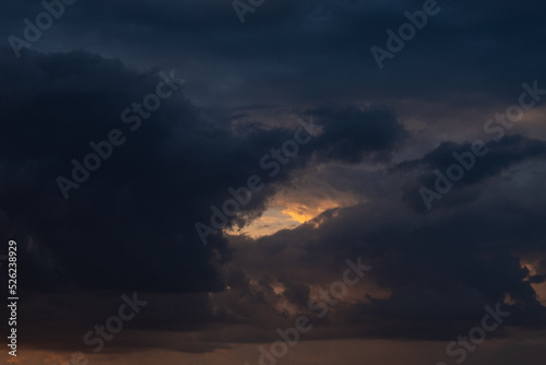 Dark storm or rain heavy clouds with golden and yellow rays of sunshine passing through them. Gloomy. Background. Nature. Horizontal photo. 