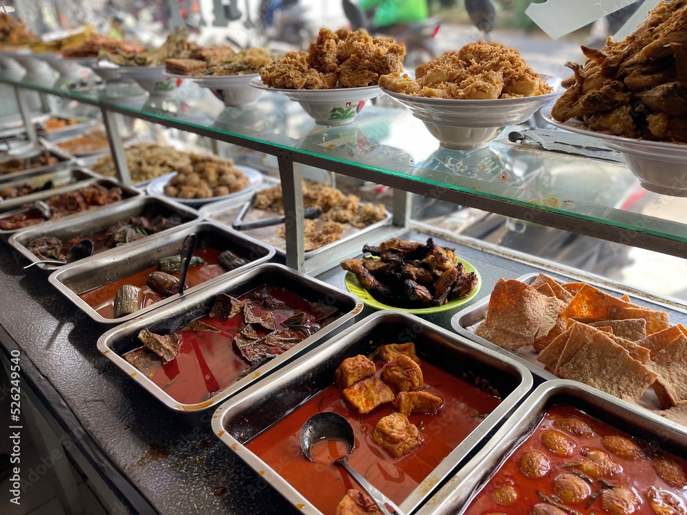 Fototapeta premium Padang food stalls share a variety of buffet menus with vegetables, chicken curry sauce, beef, eggs, tofu, tempeh. the waiter prepares the arrangement of the food. Menu in glass display case.