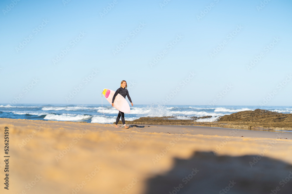 Surfer woman at the beach walking with her surfboard in the morning. Female surfer woman Surfer woman at the beach walking with her surfboard in the morning. Female surfer woman