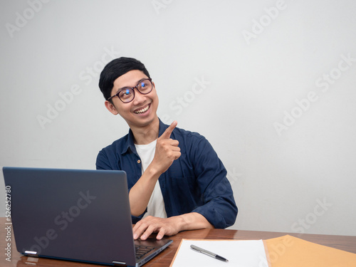 Positive man wear glasses point finger and sit at working table