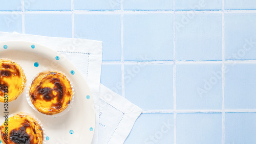 Traditional Portuguese egg tart dessert Pasteis Pastel de nata or Pastels de Belem on the plate on blue tile. Flat lay with copy space