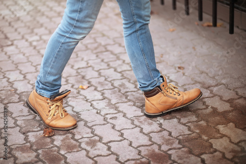 Autumn concept. Pedestrian feet on the road. Autumn leaves on the footpath.