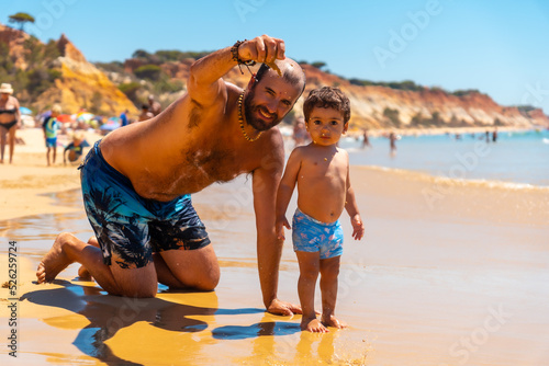 Father playing in the sand with son, Praia do Barranco das Belharucas beach, Albufeira, Algarve. Portugal photo