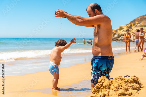 Father playing in the sand and having fun with son, Praia do Barranco das Belharucas beach, Albufeira, Algarve. Portugal photo