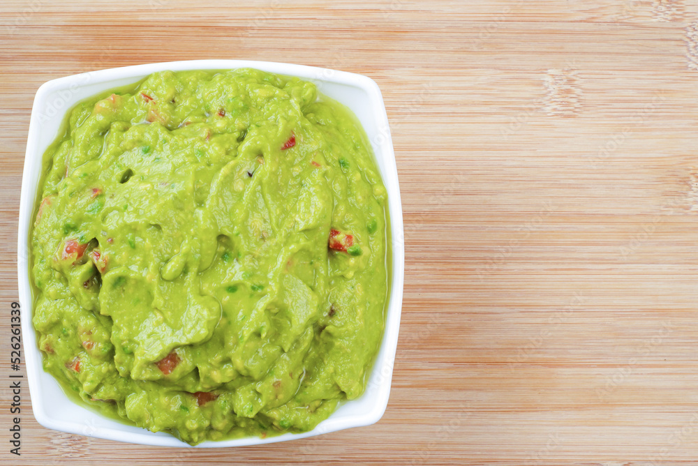 Guacamole served on white plate on wooden table. Insulated container with guacamole. Guacamole served on white plate on wooden table. Insulated container with guacamole.