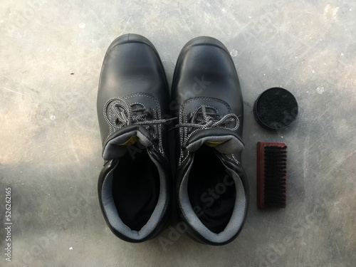 Black safety shoes next to a shoe brush and shoe polish. Ready to go to work photo