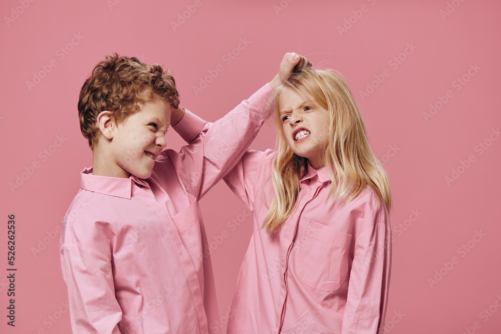 school-age children a boy and a girl have quarreled and stand holding each other by the hair standing on a pink background in pink clothes menacingly looking at each other school-age children a boy and a girl have quarreled and stand holding each other by the hair standing on a pink background in pink clothes menacingly looking at each other