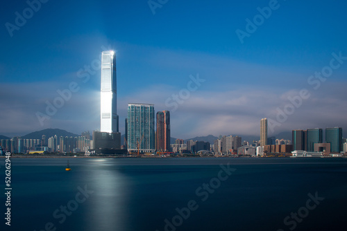 Lighthouse.  The sun reflects off a skyscraper on Kowloon  Hong Kong casting light over the blue sea.  Long exposure gives a silky smooth sea.