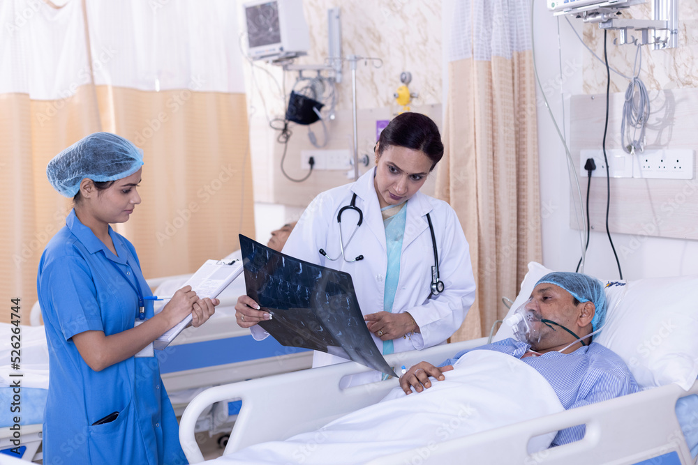 Female doctor explaining Xray to male patient lying on bed during medical treatment. Young nurse is writing on clipboard and making reports. They are at hospital ward.
Female doctor explaining Xray to male patient lying on bed during medical treatment. Young nurse is writing on clipboard and making reports. They are at hospital ward.