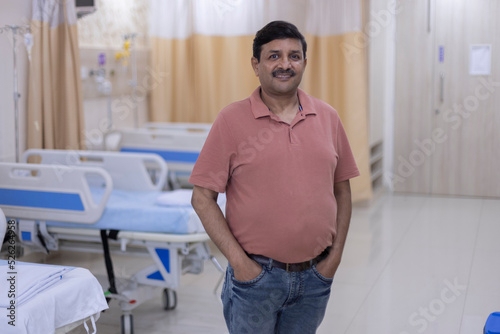 Portrait of confident senior man standing at hospital ward 