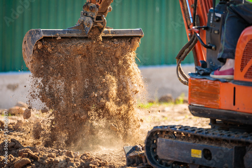 A minitractor rakes the earth with a bucket. Land works. photo